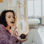 donna seduta sul divano che mangia un muffin