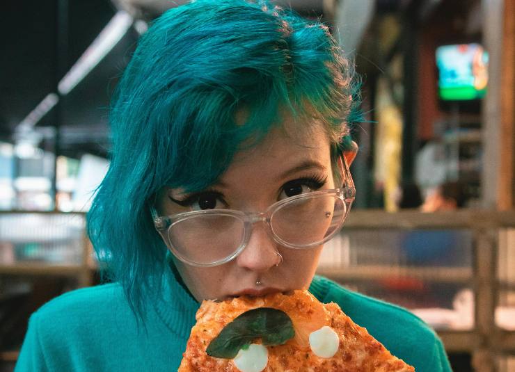 ragazza che mangia una fetta di pizza