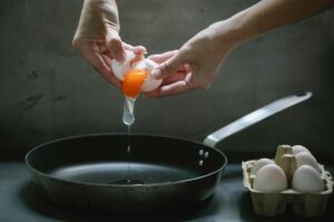 Persona che apre un uovo e lo fa cadere in padella